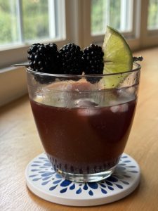 dark colored mocktail in a glass garnished with blackberries and lime